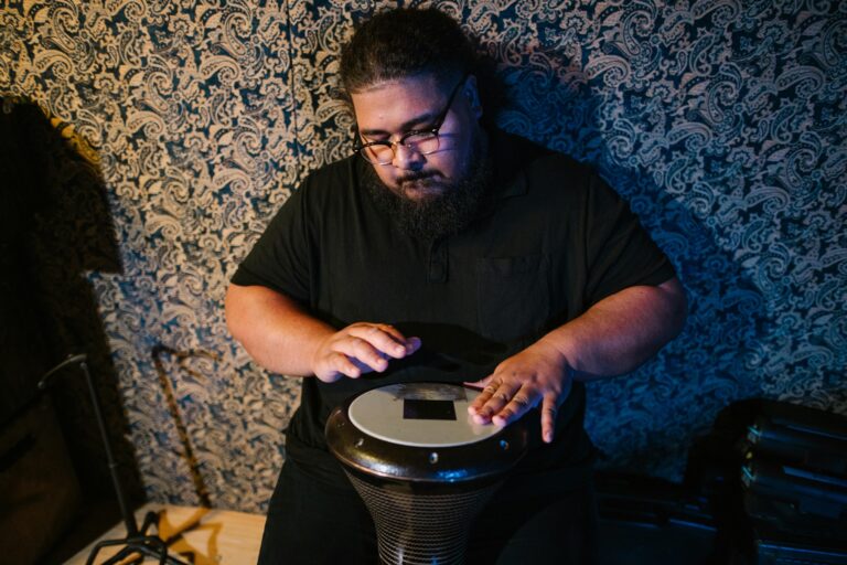 An adult musician skillfully plays a hand drum in an indoor studio setting.