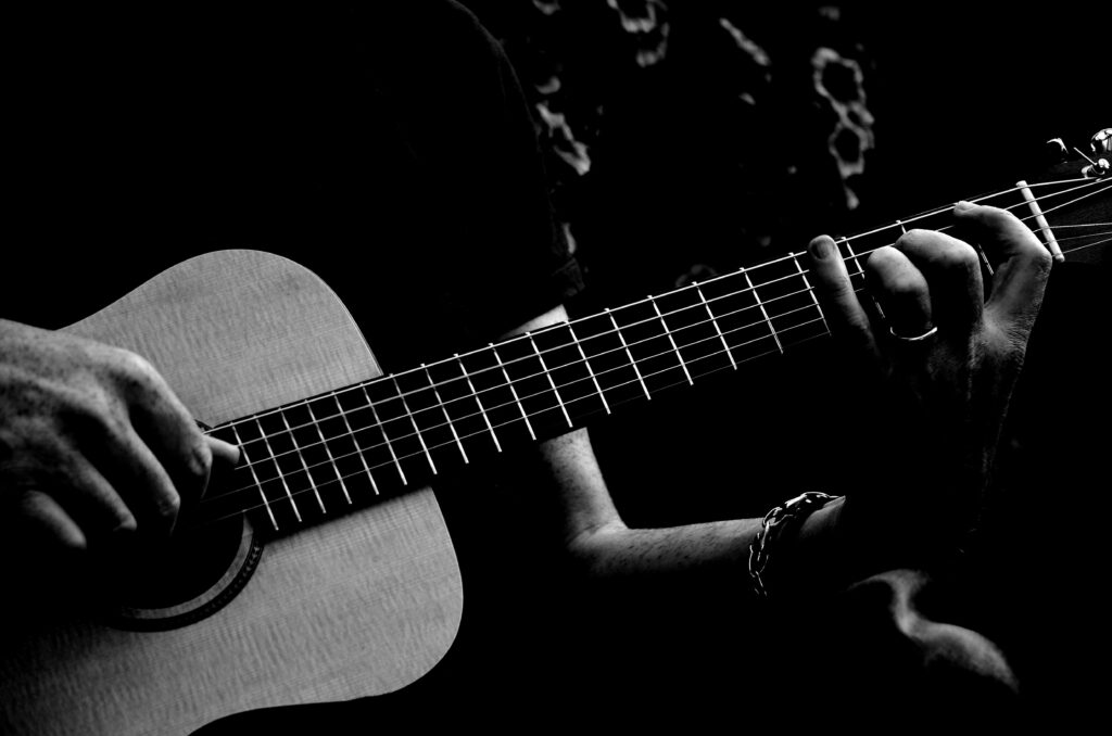 Black and white image of a person strumming an acoustic guitar, focusing on hands.