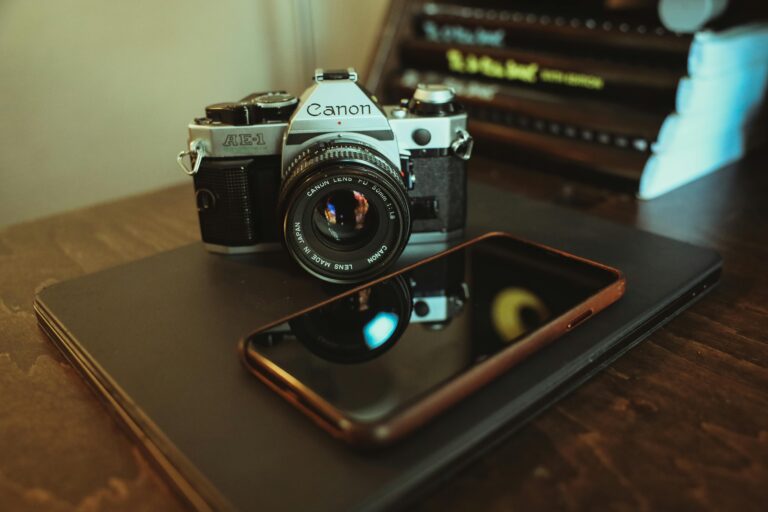 Close-up of a vintage camera, smartphone, and laptop on a wooden table.