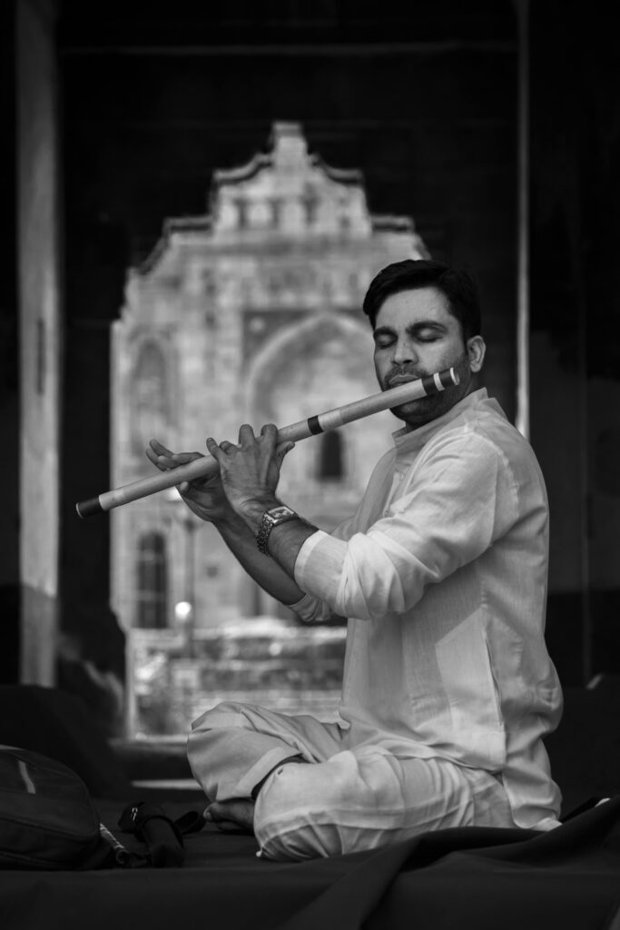 A man in traditional attire playing the flute with closed eyes in a serene setting.