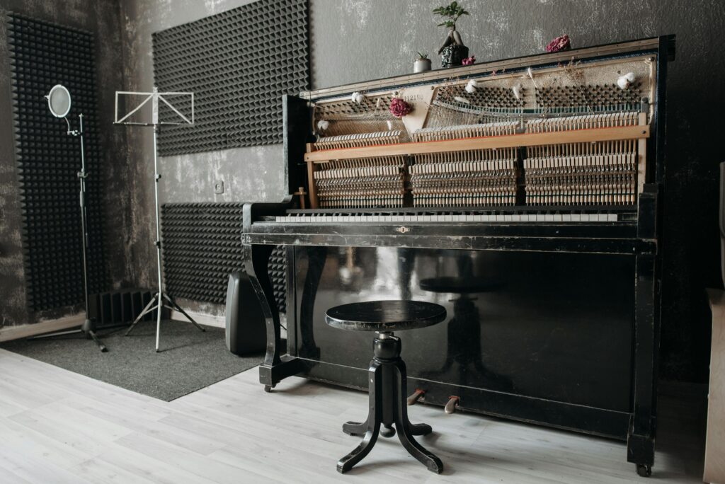 An open vintage upright piano in a soundproof music studio with recording equipment.